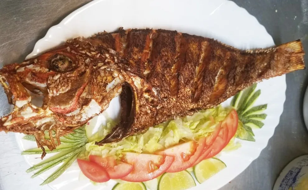 A whole fried fish on a white platter with sliced tomato, lettuce and lime